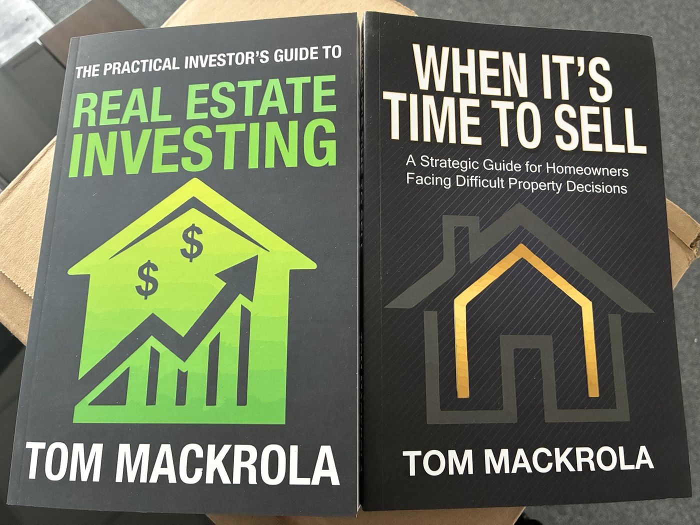 Printed copies of The Practical Investor's Guide to Real Estate Investing and When It's Time to Sell resting on a shipping box